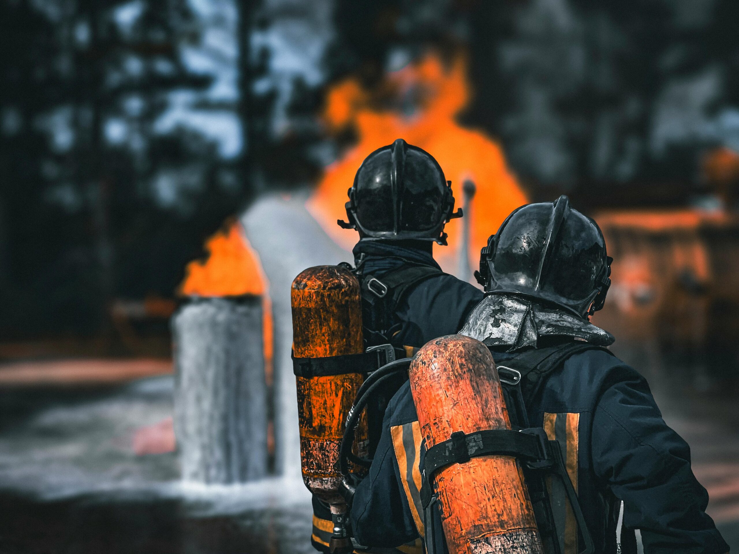 Two firefighters in protective gear facing a large blaze with determination outdoors.